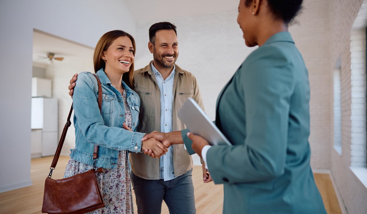 Happy woman shaking hands with real estate agent while buying new apartment with her husband.